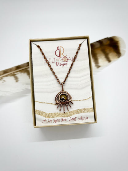 Copper eye-shaped pendant necklace with a golden Tiger’s Eye gemstone in a Built to Roam Designs jewelry box against a white background - front view - Guardian