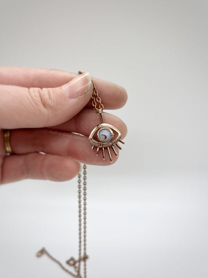 Hand holding a Copper eye-shaped pendant necklace with a blue lace agate gemstone against a white background - front view - Comfort