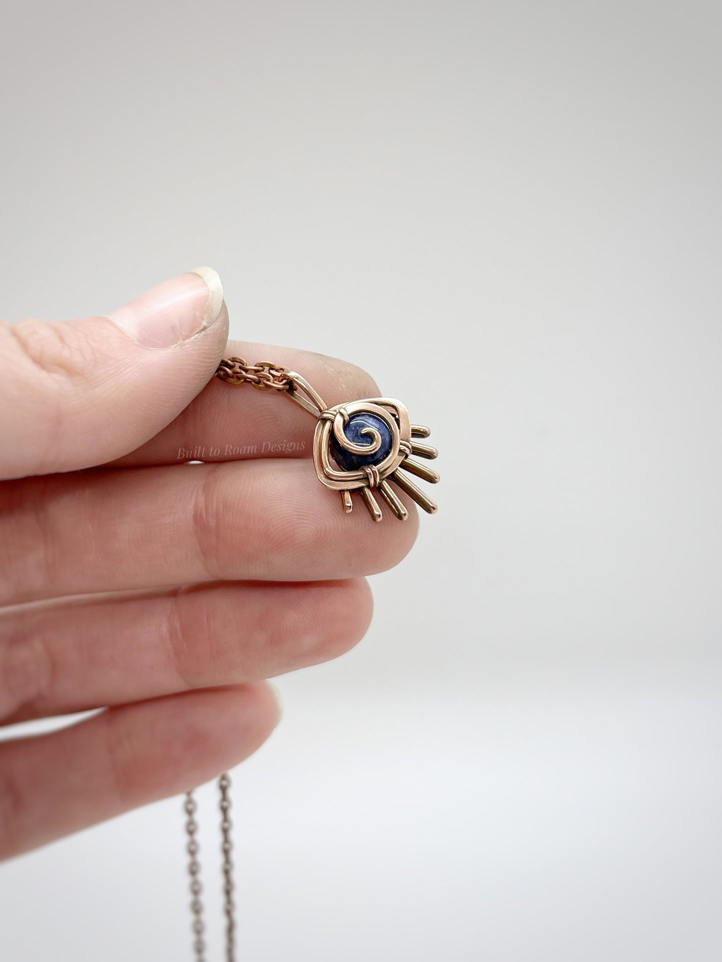 Copper eye-shaped pendant necklace with a blue Sodalite gemstone against a white background - side view - Insight