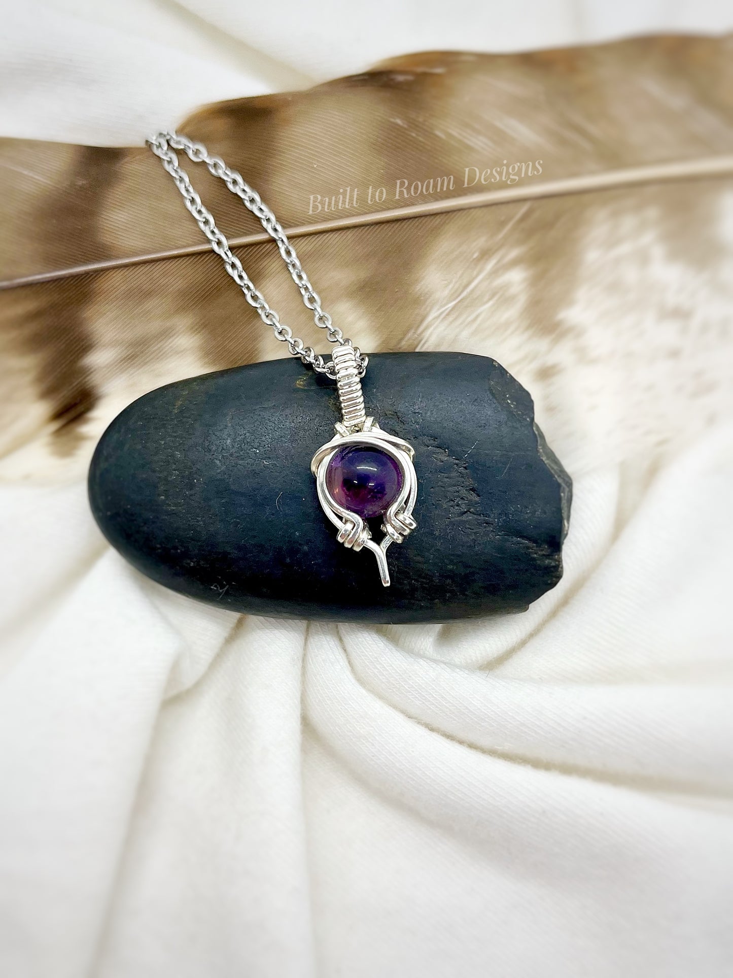 Silver necklace with a purple amethyst gemstone pendant on a black stone