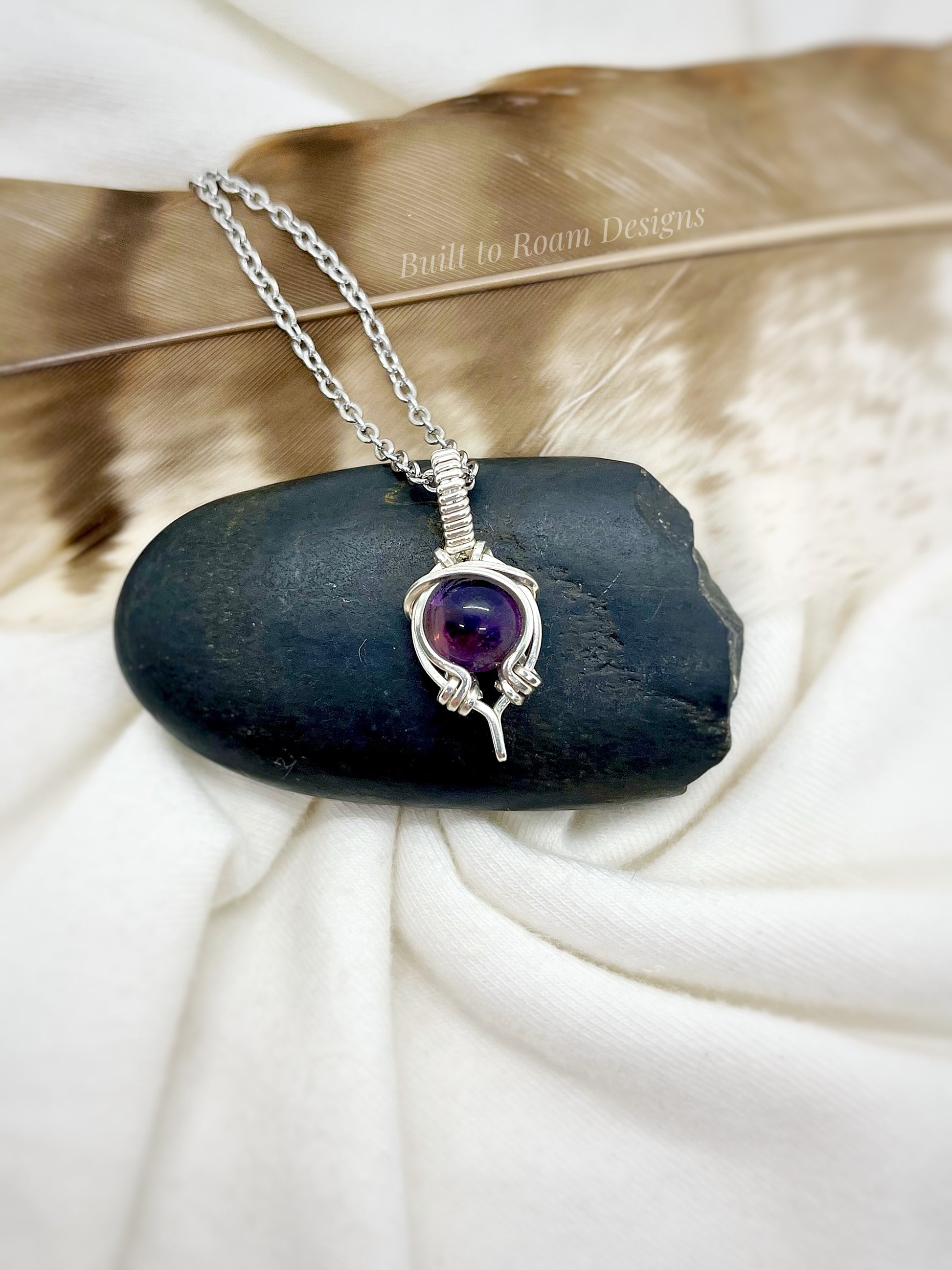 Silver necklace with a purple amethyst gemstone pendant on a black stone