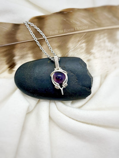 Silver necklace with a purple amethyst gemstone pendant on a black stone