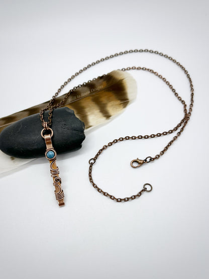 Swirly copper bar necklace with a blue Larimar bead on a rock with white background - front view - Current