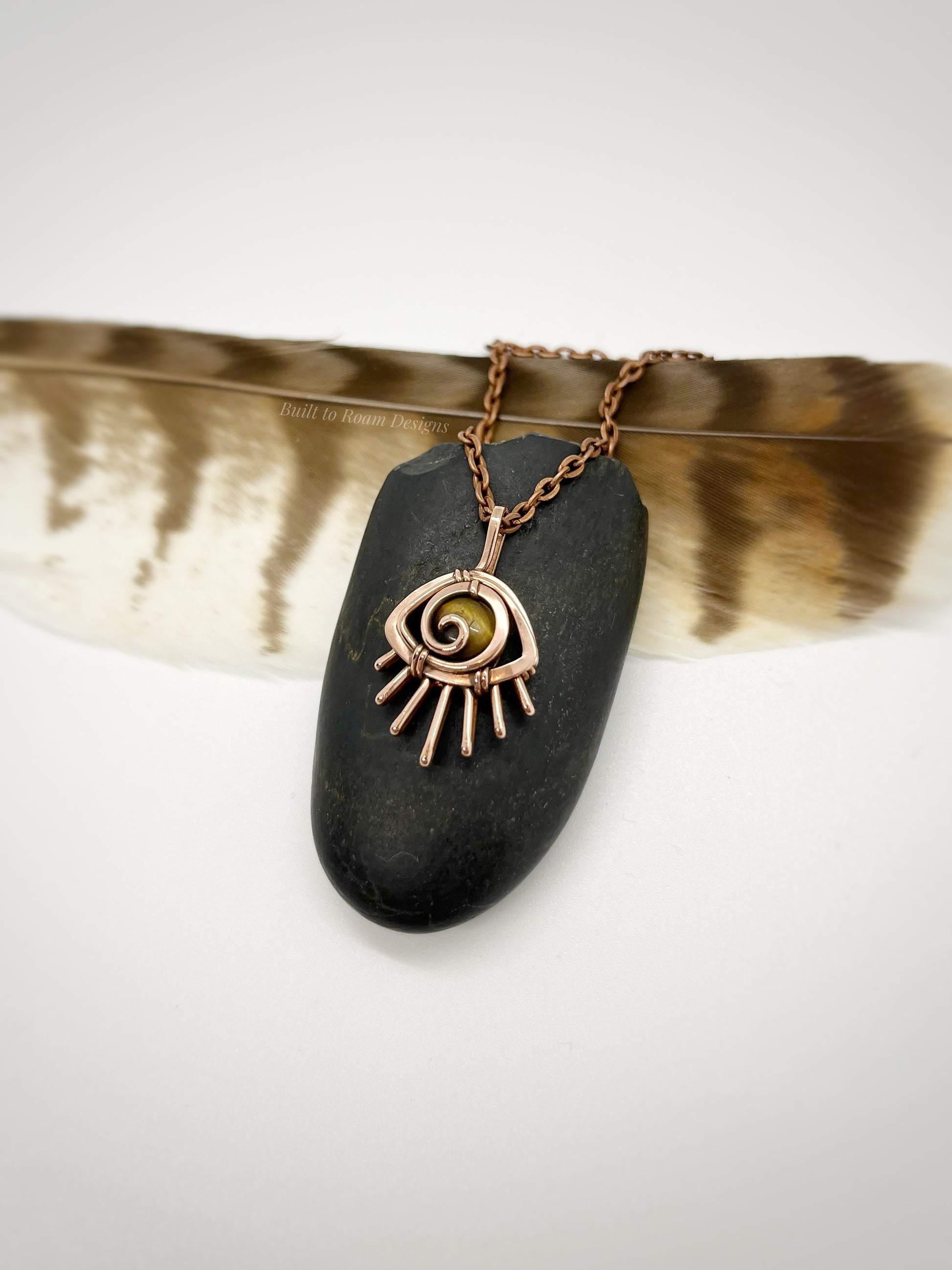 Copper eye-shaped pendant necklace with a golden Tiger’s Eye gemstone against a dark stone - side view - Guardian