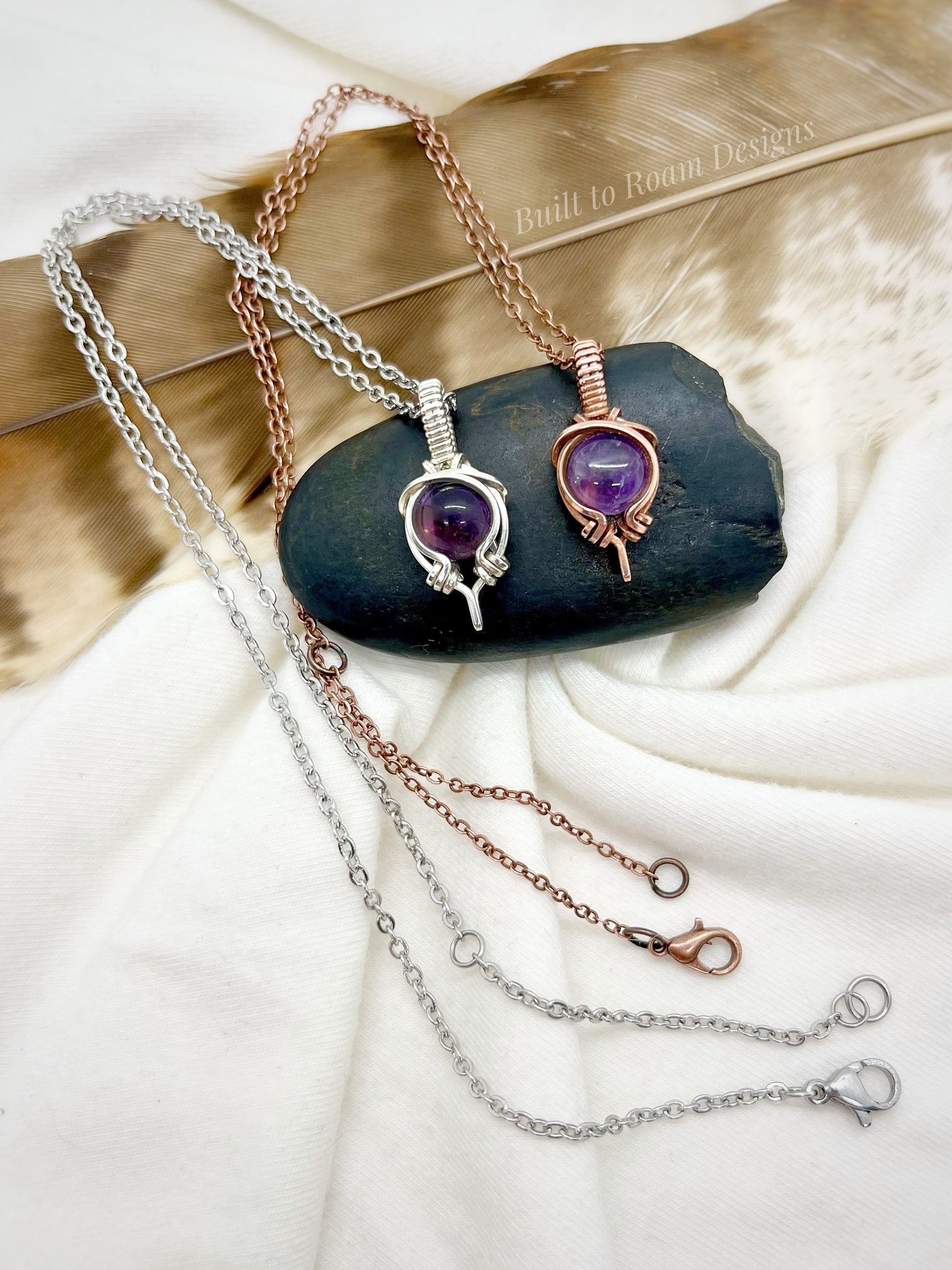 Two purple amethyst pendants on necklaces on a dark stone surface with white background