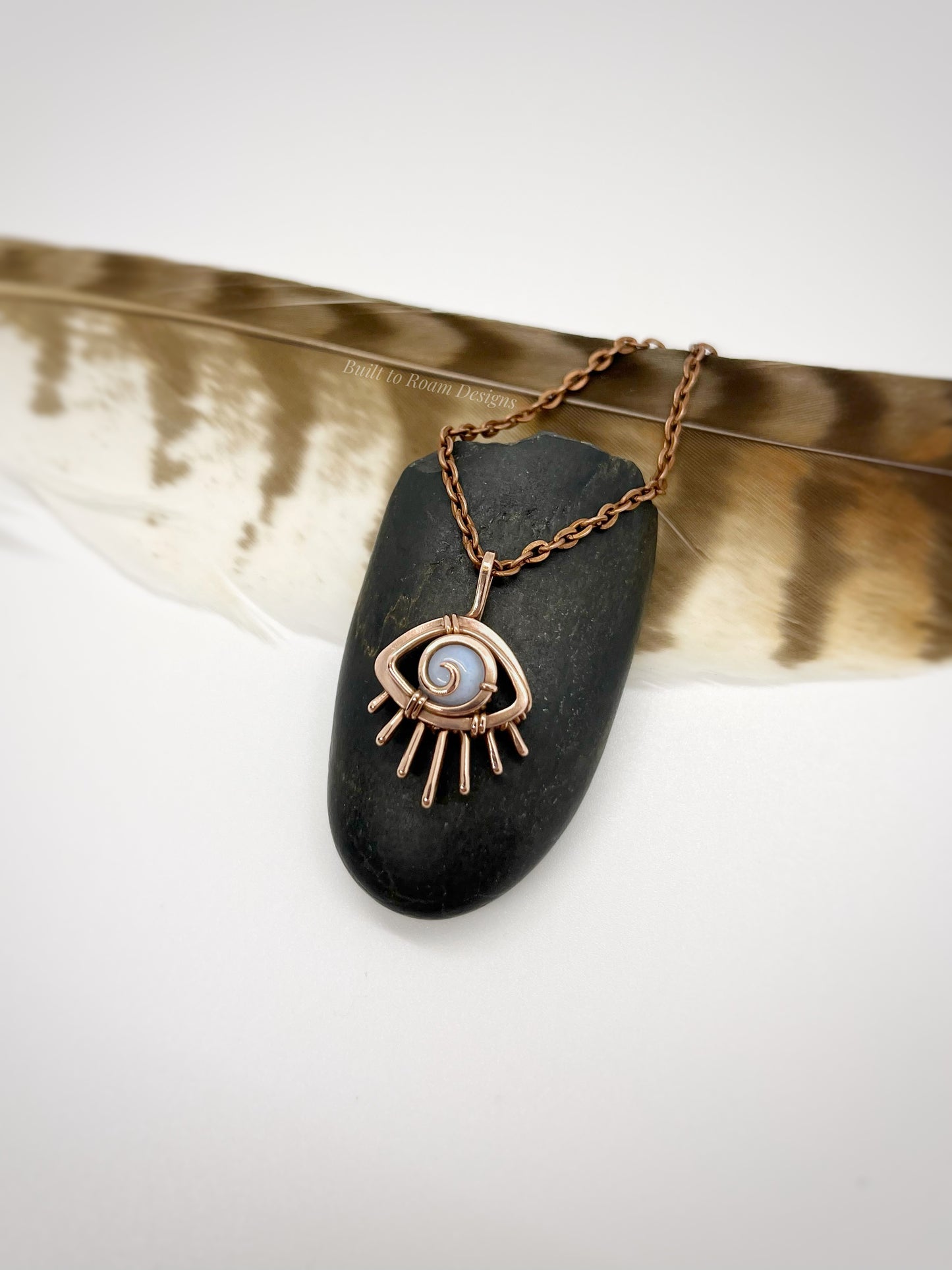 Copper eye-shaped pendant necklace with a blue lace agate gemstone against a dark stone with white background - side view - Comfort