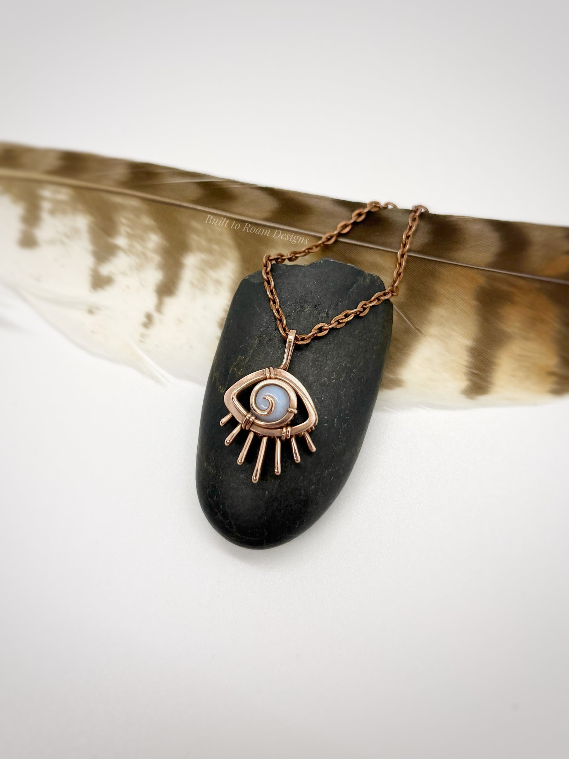 Copper eye-shaped pendant necklace with a blue lace agate gemstone against a dark stone with white background - side view - Comfort