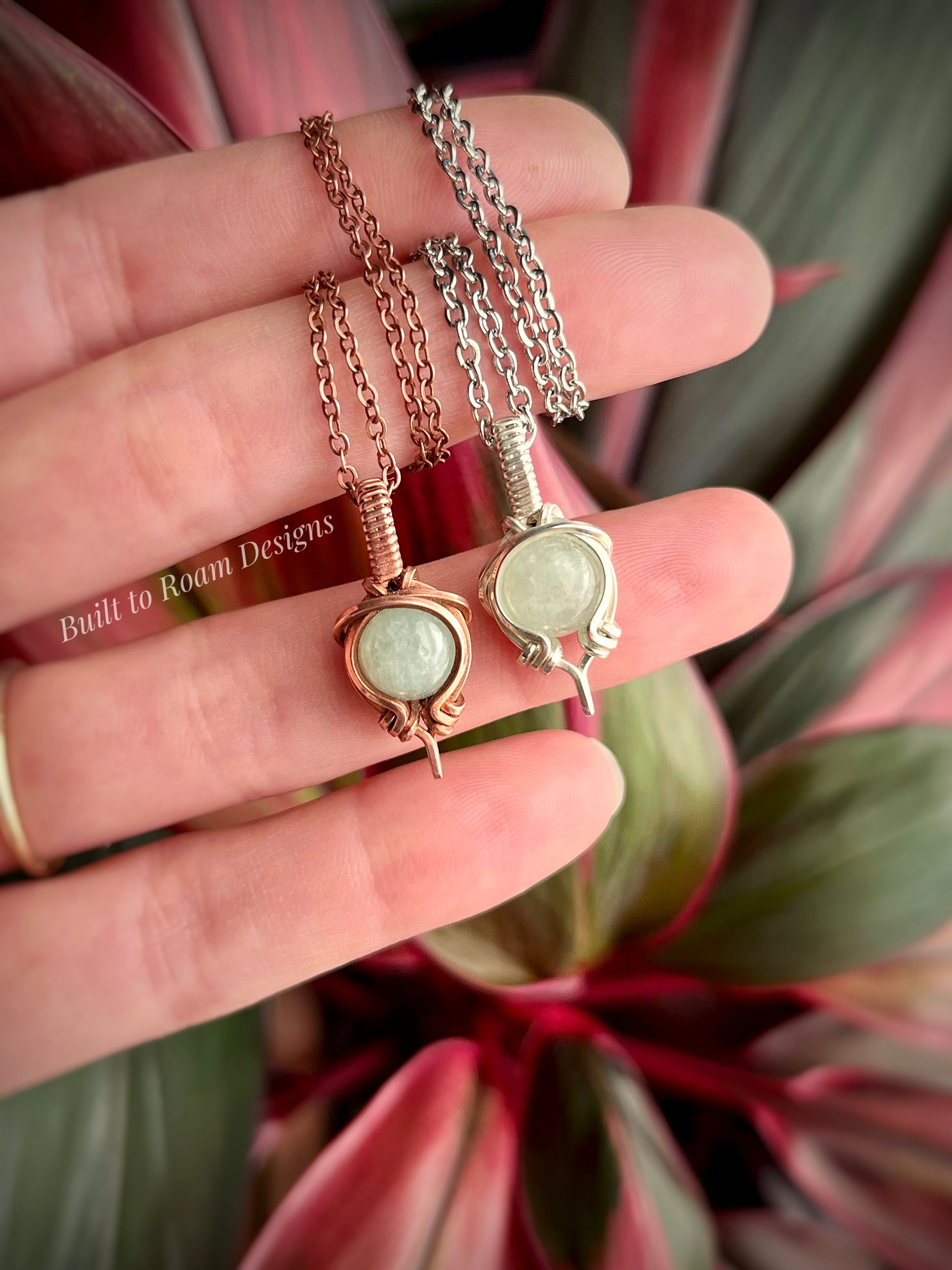 Two necklaces with green aventurine pendants held by a hand against a plant background
