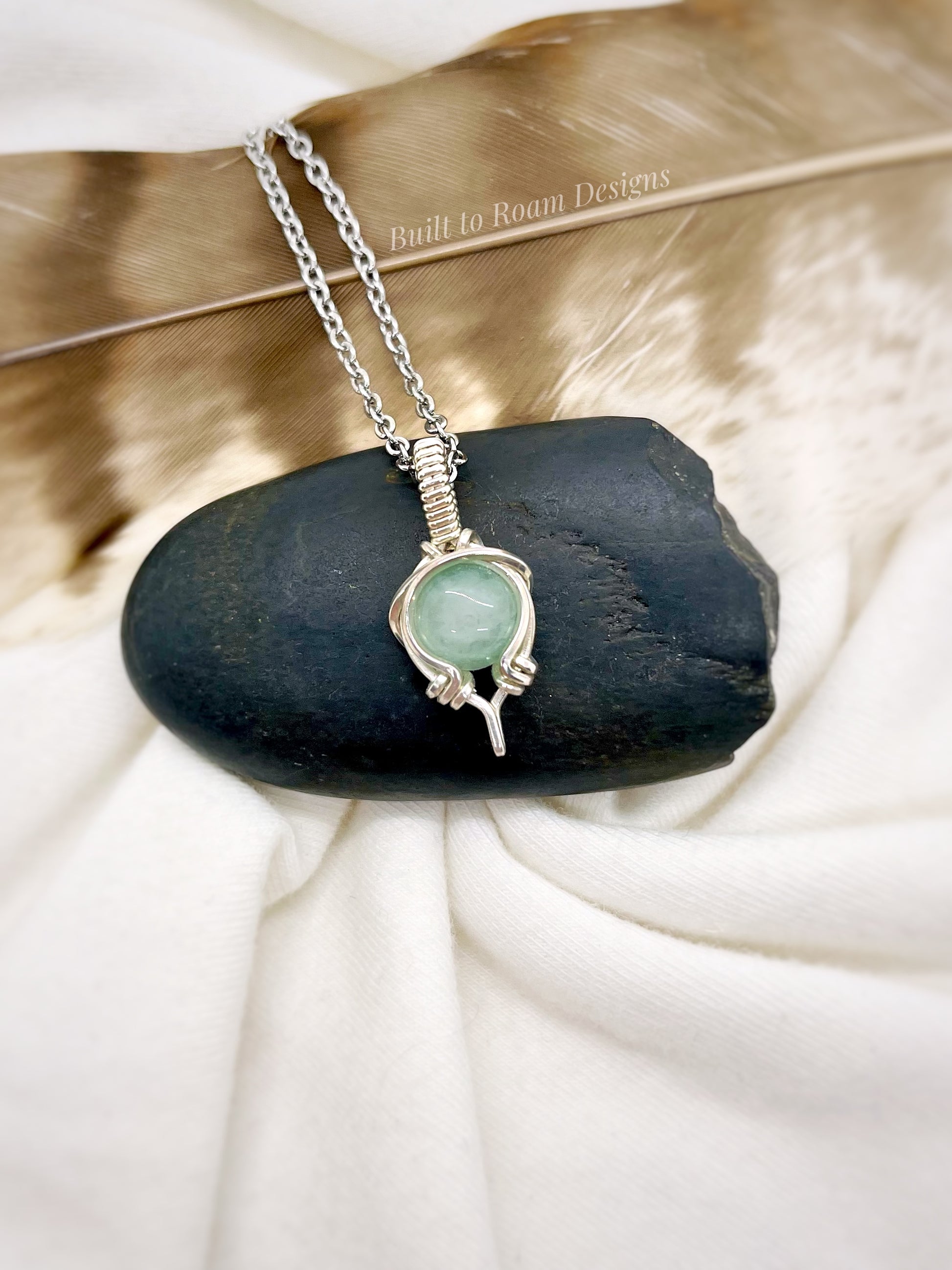 Silver Necklace with a green aventurine pendant on a dark stone against a white fabric background