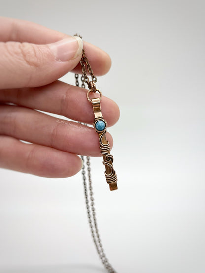 Hand holding a swirly copper bar necklace with a blue Larimar bead with white background - front view - Current