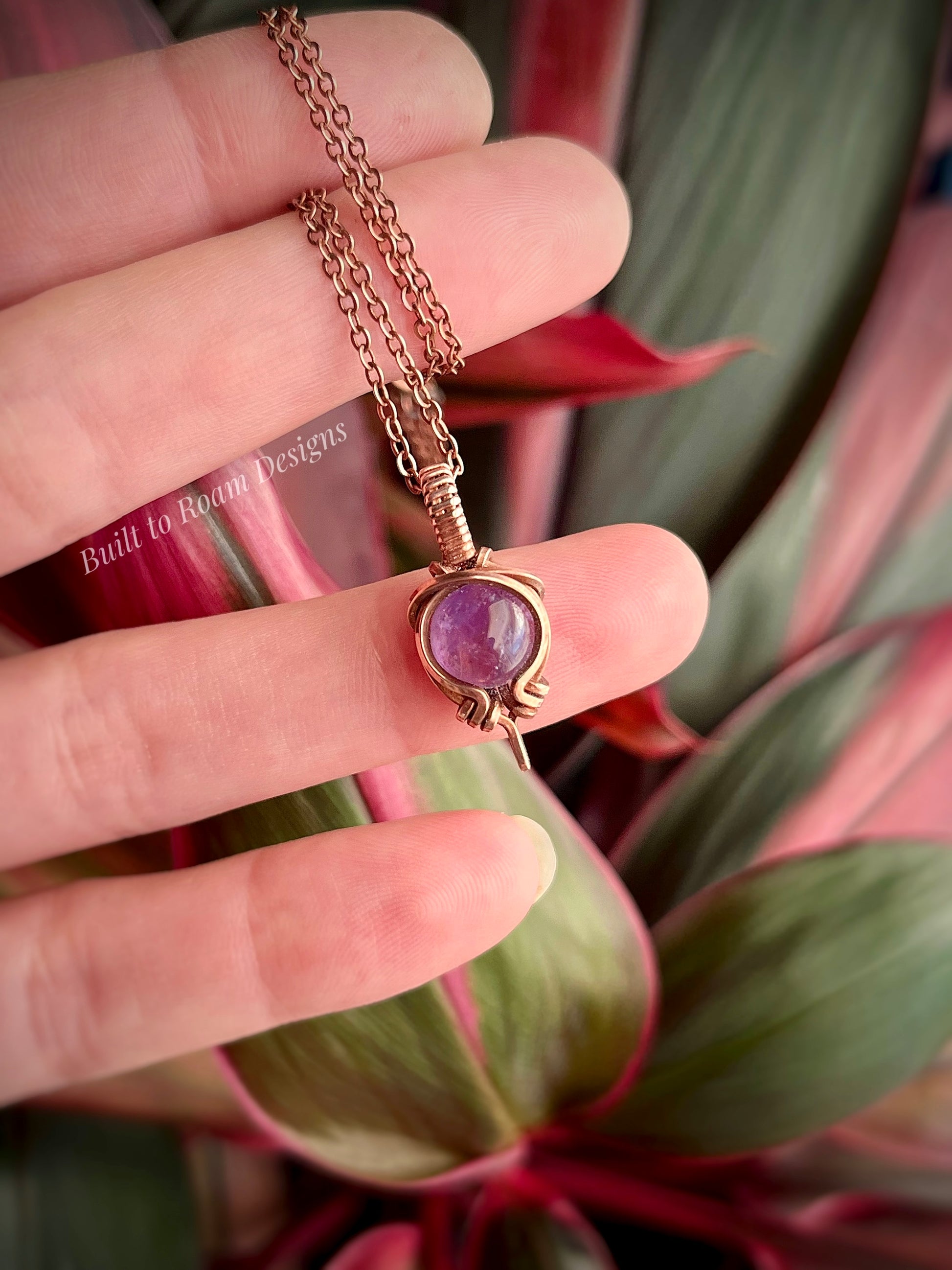 Copper Necklace with a purple amethyst gemstone pendant held between fingers against a plant background
