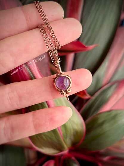 Copper Necklace with a purple amethyst gemstone pendant held between fingers against a plant background