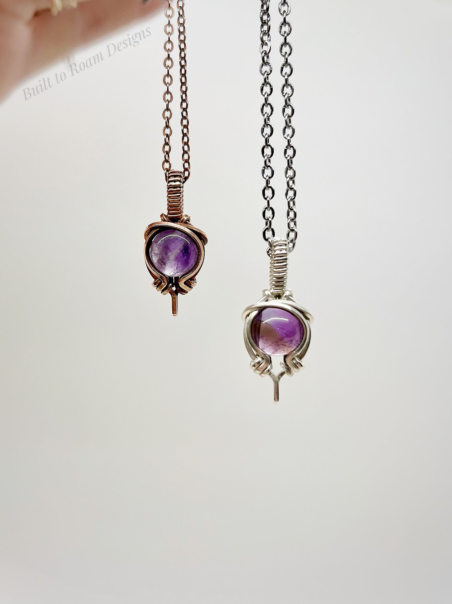 Two purple amethyst pendants on chains against a white background