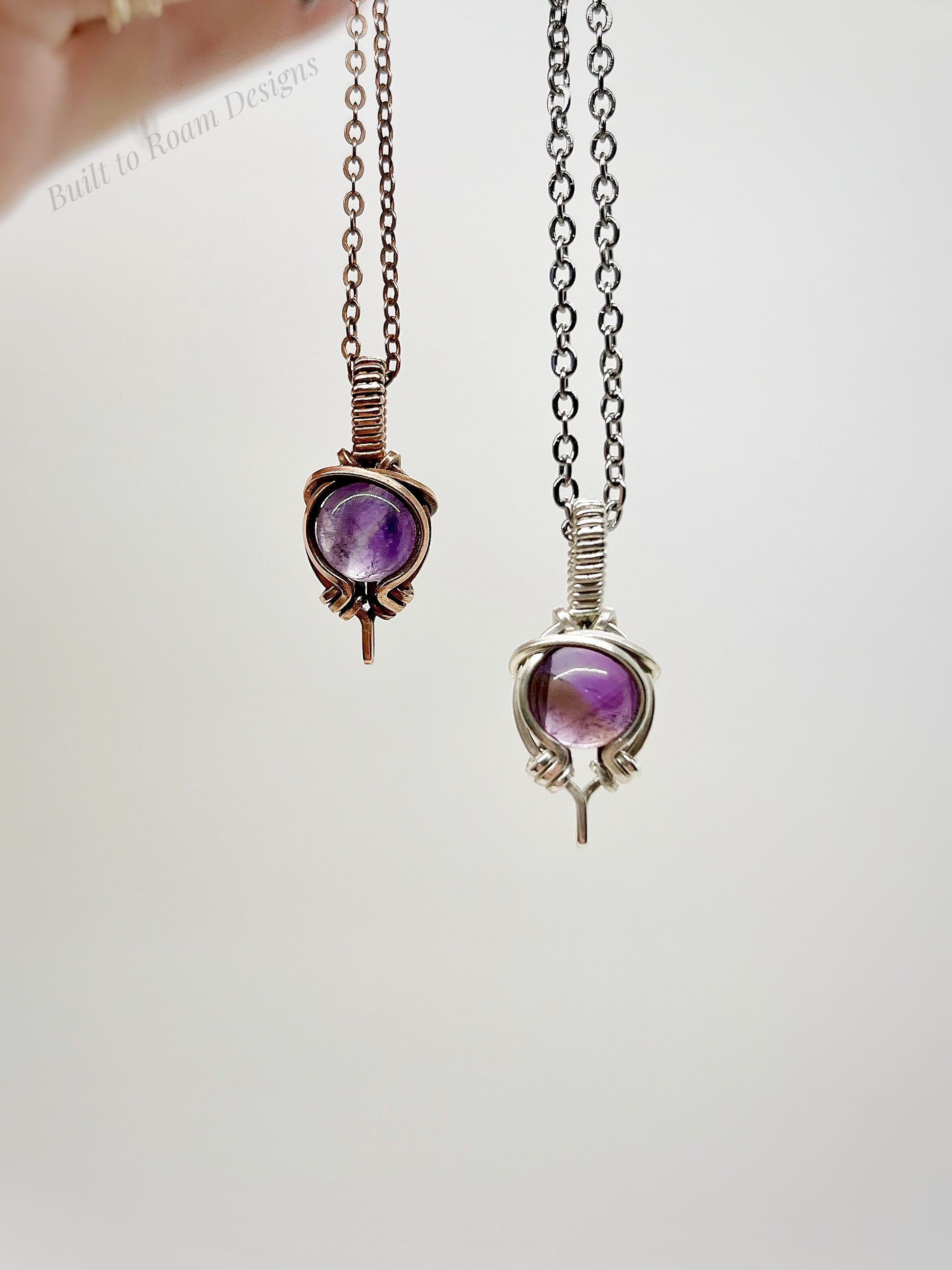 Two purple amethyst pendants on chains against a white background