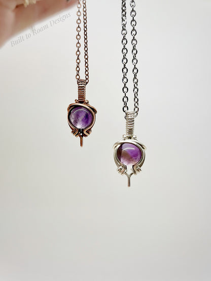 Two purple amethyst pendants on chains against a white background