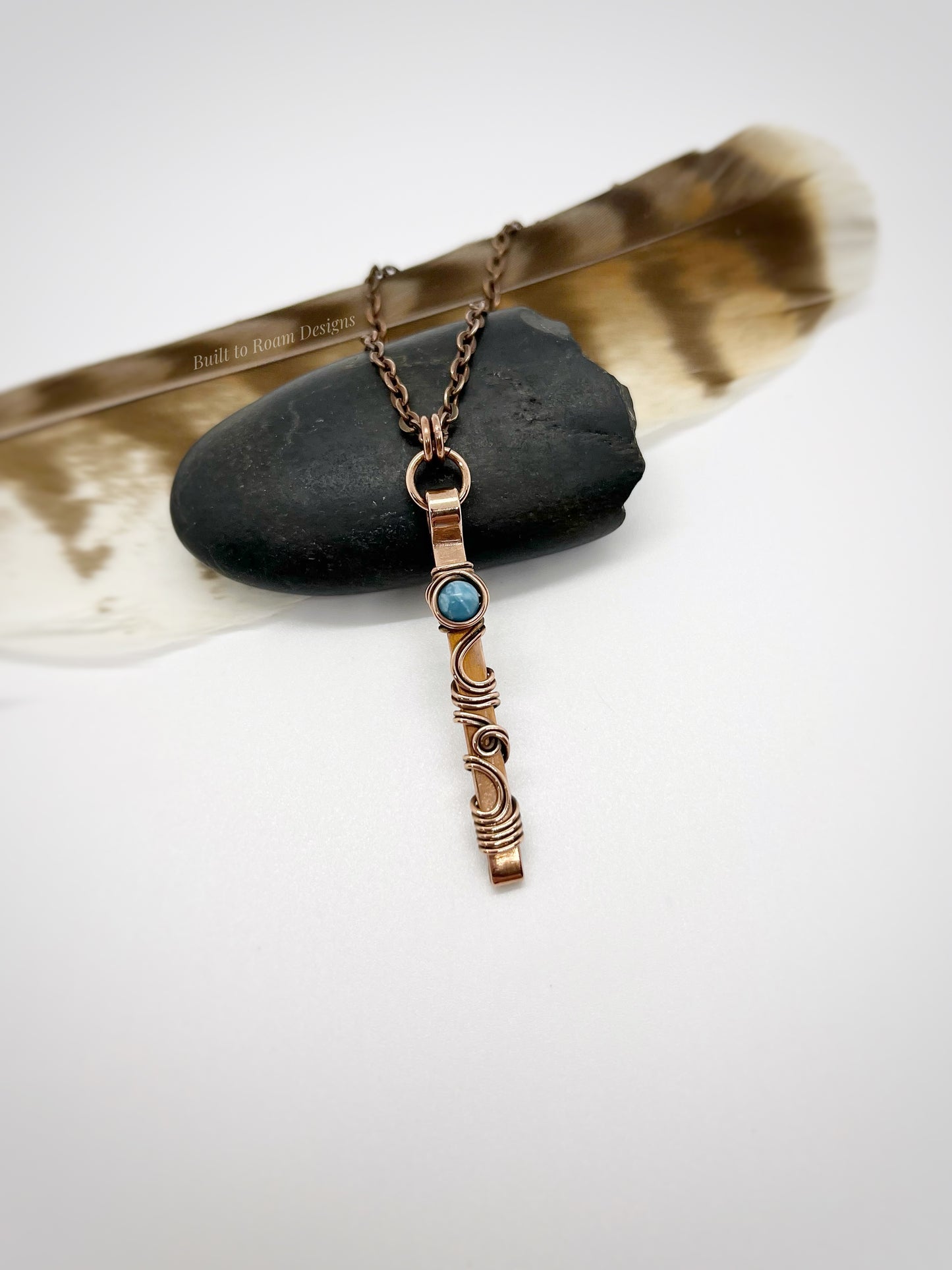 Swirly copper bar necklace with a blue Larimar bead on a rock with white background - front view - Current