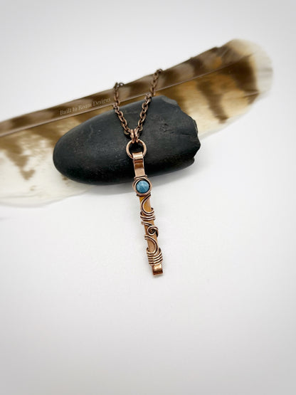 Swirly copper bar necklace with a blue Larimar bead on a rock with white background - front view - Current