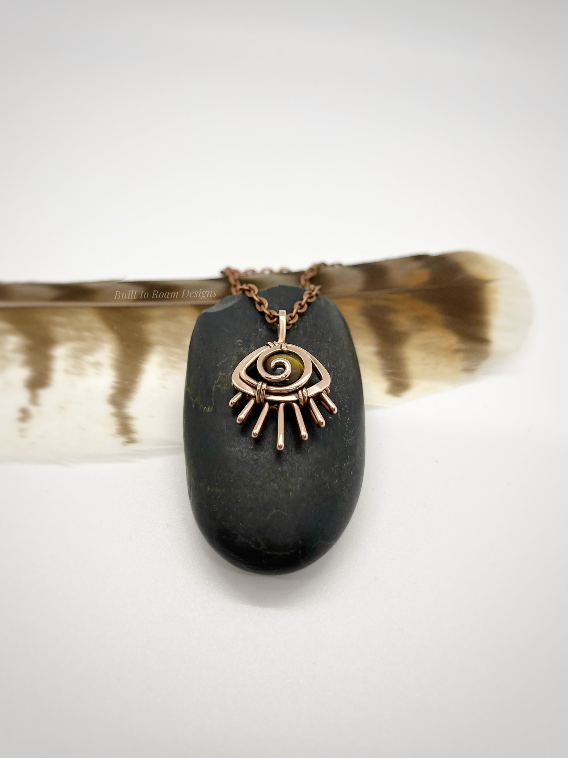Copper eye-shaped pendant necklace with a golden Tiger’s Eye gemstone against a dark stone - side view - Guardian