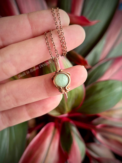 Copper Necklace with a green aventurine gemstone pendant held between fingers against a plant background
