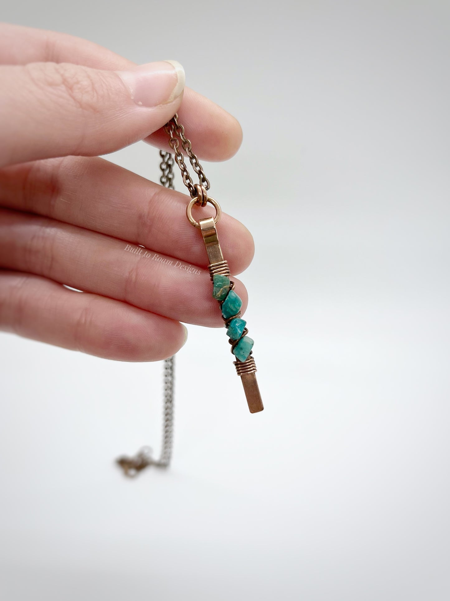 Hand holding a Copper bar necklace with teal amazonite chip beads with white background - front view - Origin