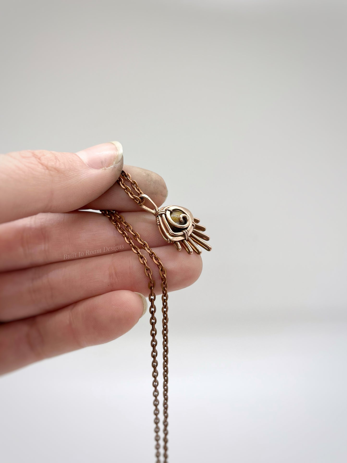 Hand holding a Copper eye-shaped pendant necklace with a golden Tiger’s Eye gemstone against a white background - front view - Guardian