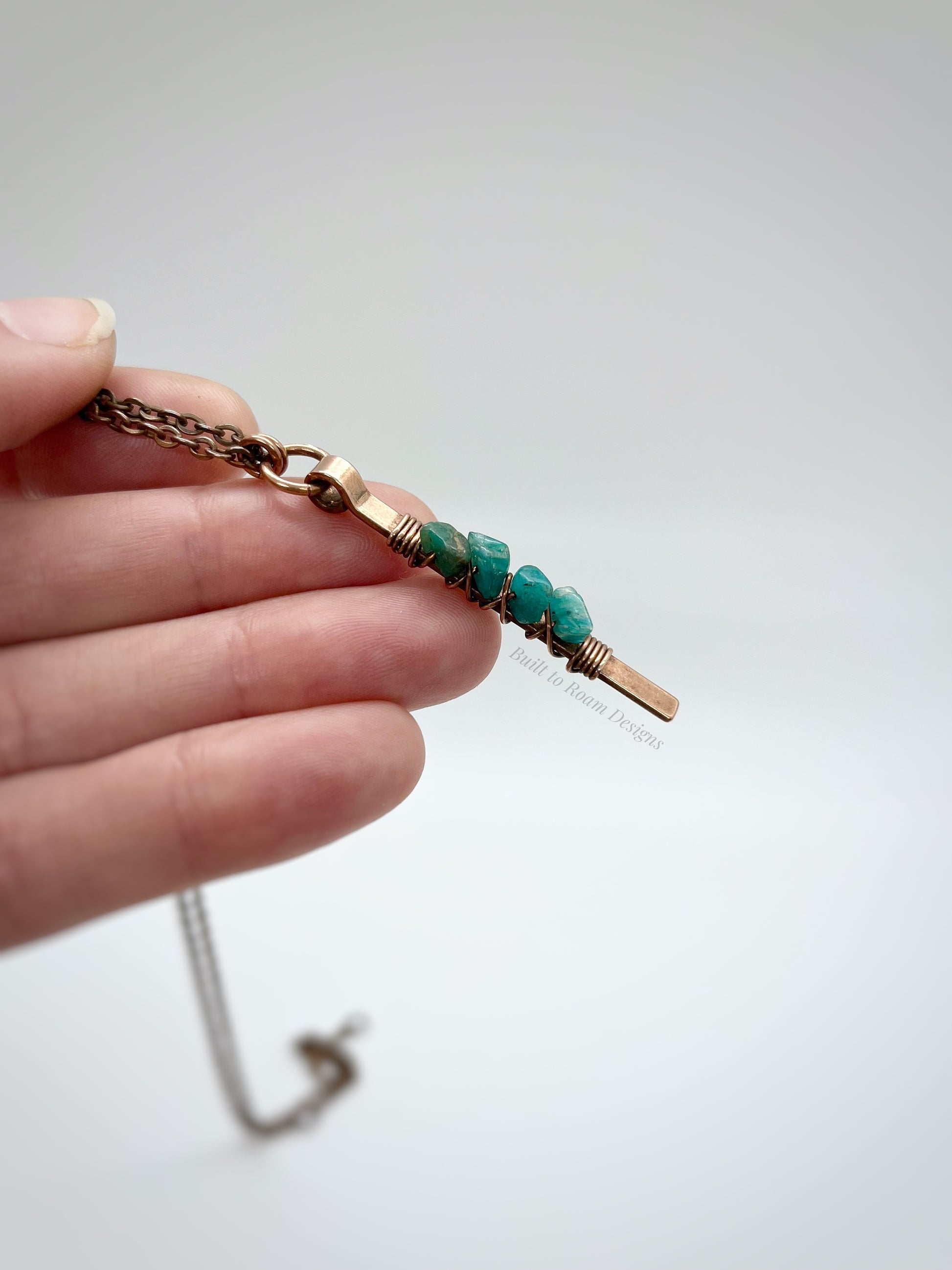 Hand holding a Copper bar necklace with teal amazonite chip beads with white background - side view - Origin