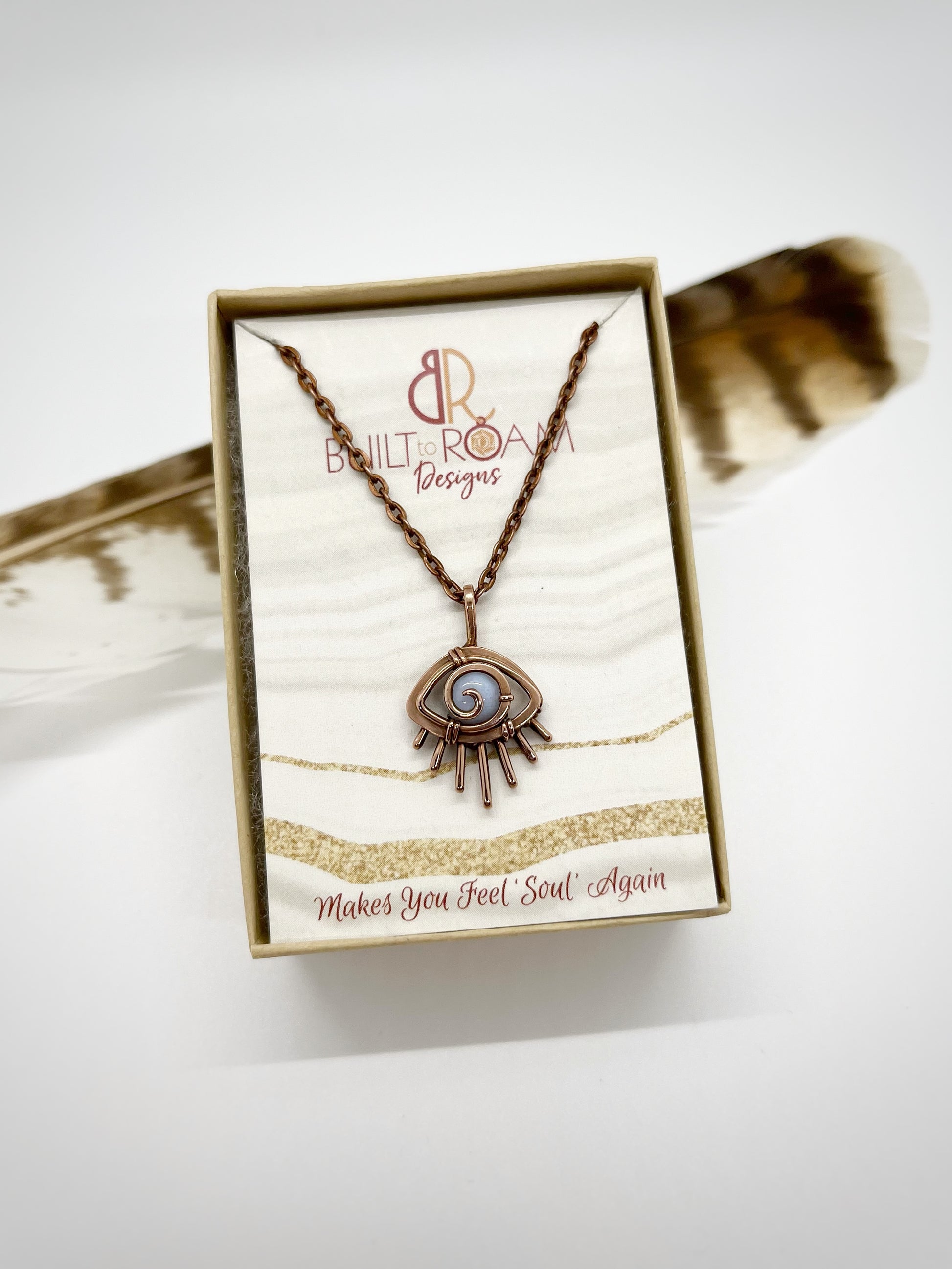 Copper eye-shaped pendant necklace with a blue lace agate gemstone in a Built to Roam Designs jewelry box with white background - side view - Comfort