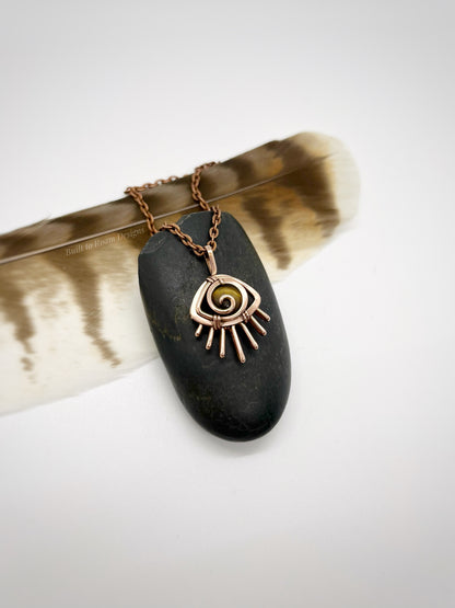 Copper eye-shaped pendant necklace with a golden Tiger’s Eye gemstone against a dark stone - side view - Guardian