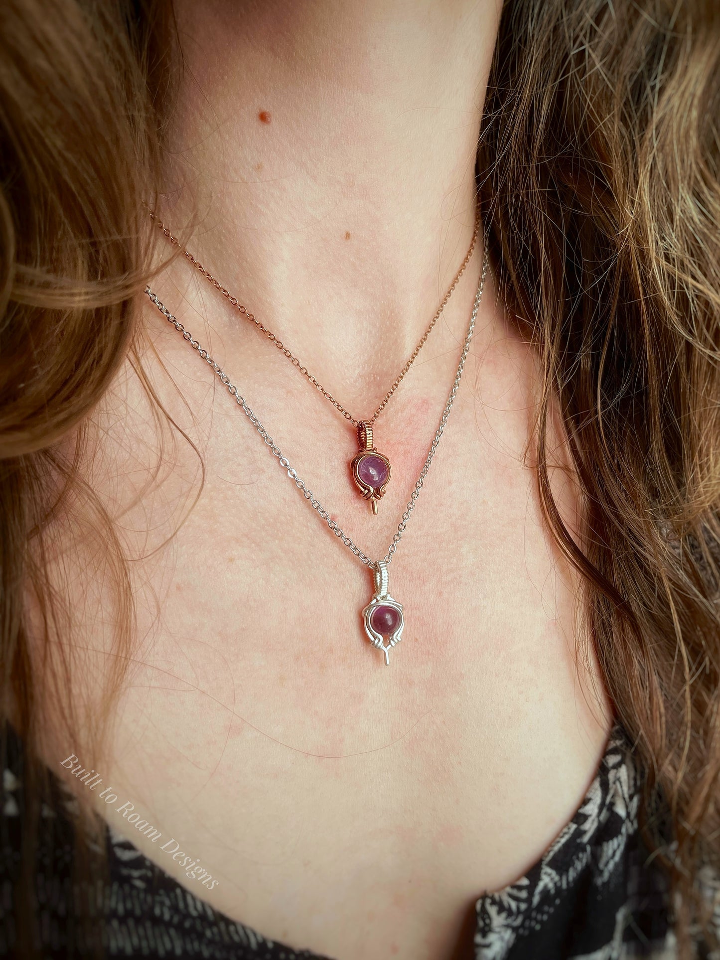 Close-up of a person wearing two necklaces with purple amethyst pendants.