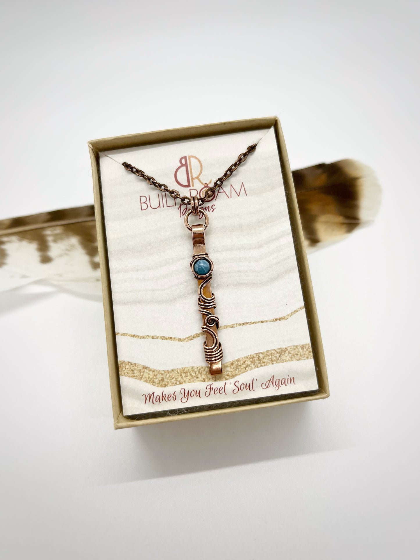 Swirly copper bar necklace with a blue Larimar bead in a But to Roam Designs jewelry box with white background - front view - Current