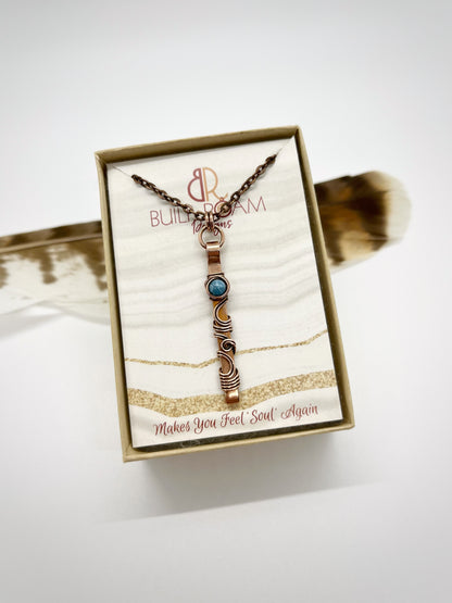 Swirly copper bar necklace with a blue Larimar bead in a But to Roam Designs jewelry box with white background - front view - Current