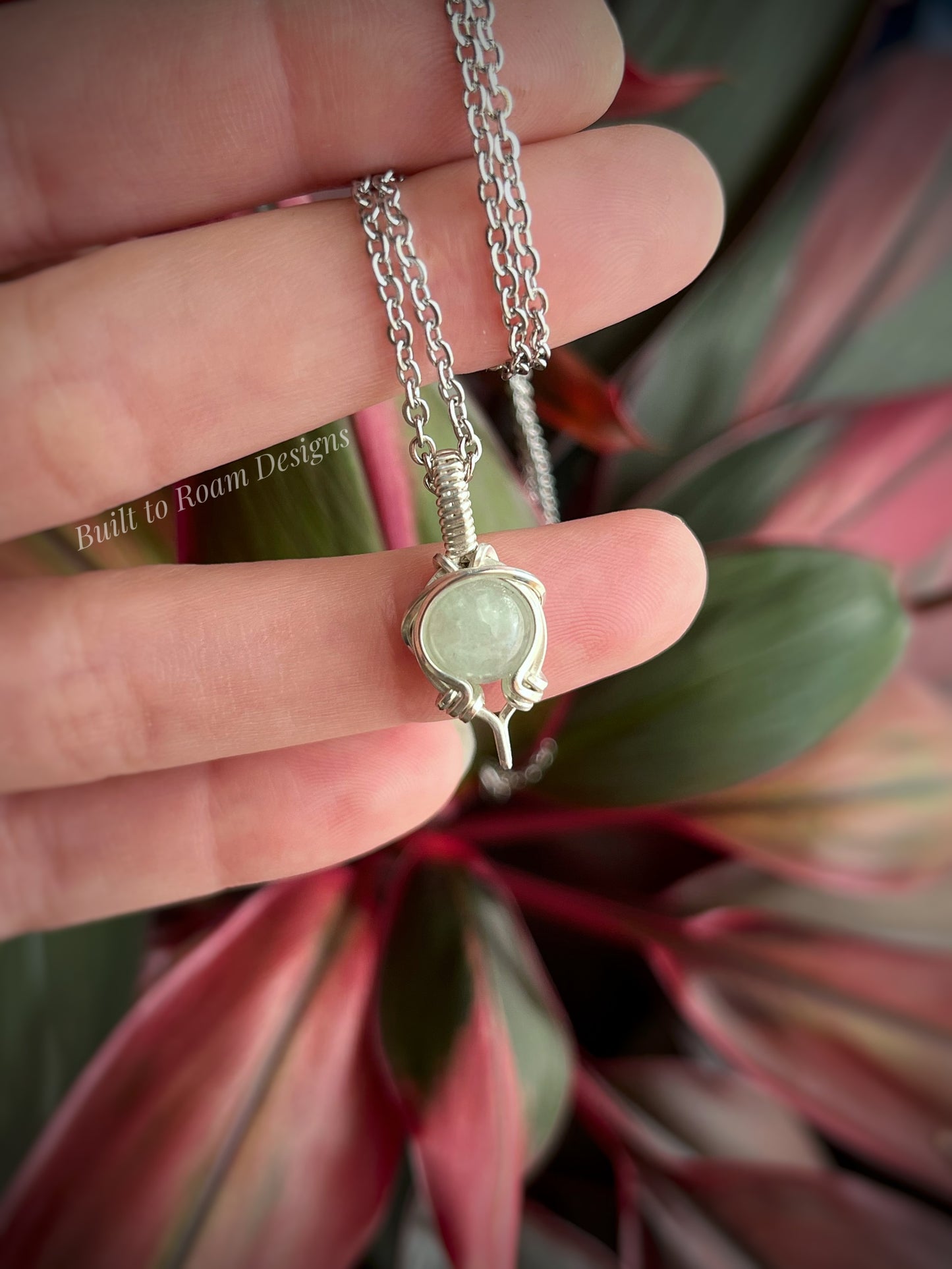 Silver necklace with a green aventurine gemstone pendant held by a hand against a plant background