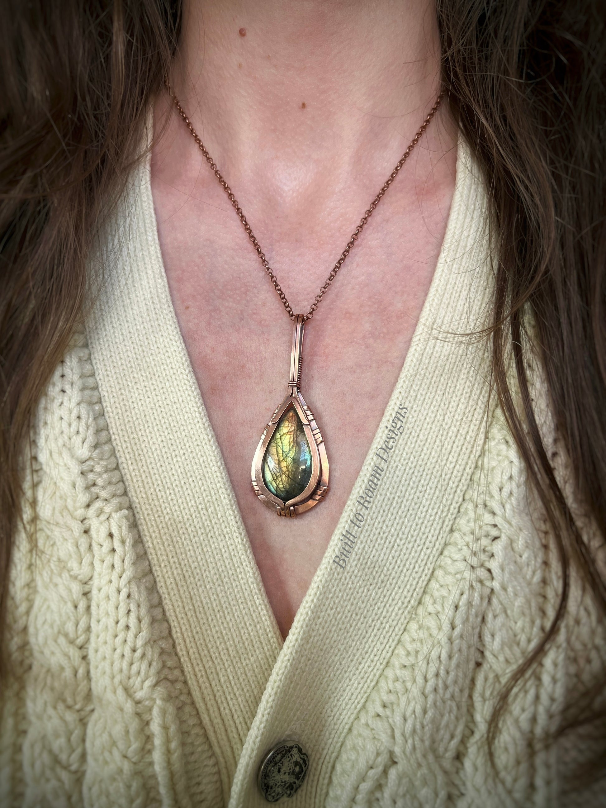 Necklace with a teardrop-shaped green labradorite pendant worn by a person in a cream sweater.