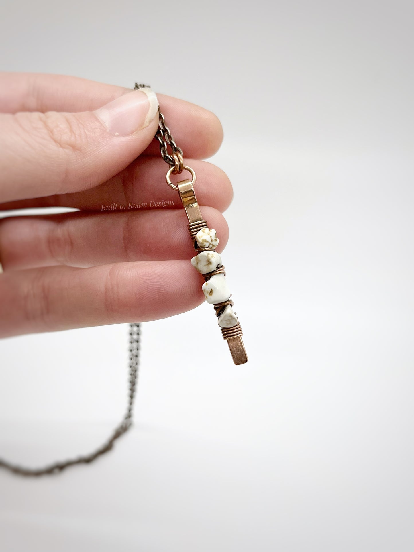 Hand holding a copper bar necklace with white turquoise chip beads on white background - front view - Horizon 