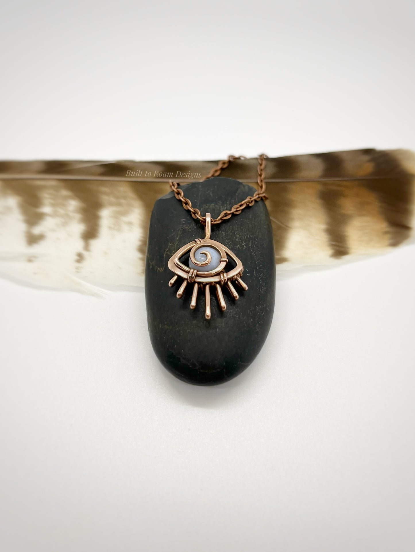 Copper eye-shaped pendant necklace with a blue lace agate gemstone against a dark stone with white background - side view - Comfort