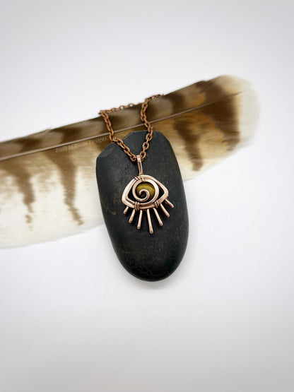 Copper eye-shaped pendant necklace with a golden Tiger’s Eye gemstone against a dark stone - front view - Guardian