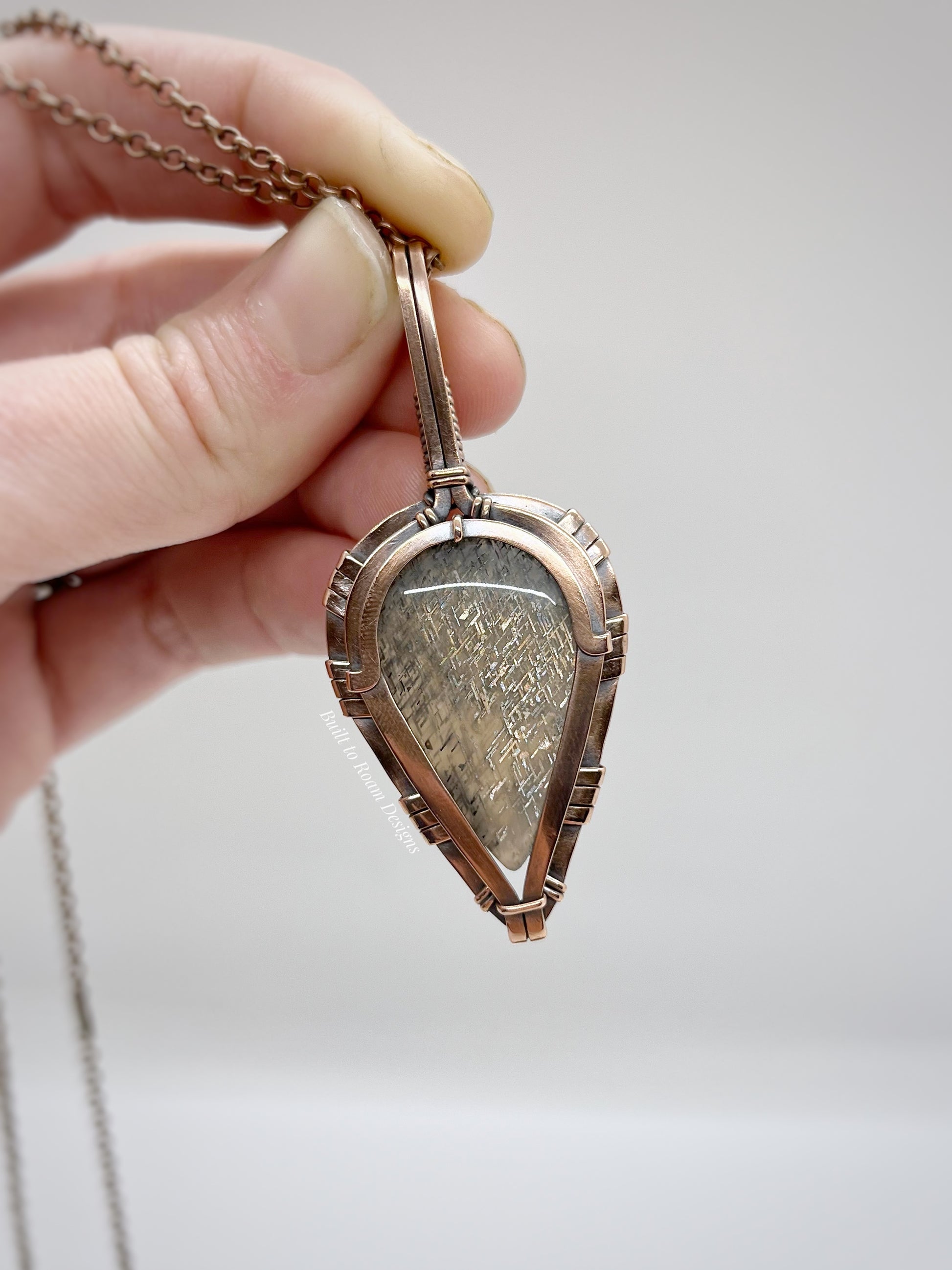 Hand holding a lattice sunstone pendant in copper against a neutral background