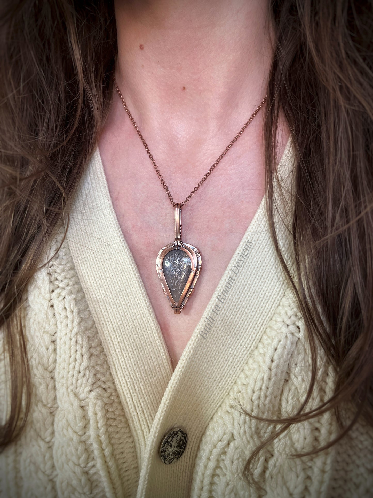 Lattice sunstone in copper pendant worn by a person in a cream sweater