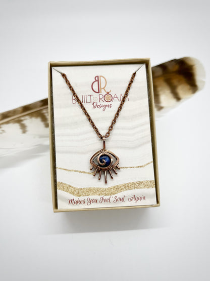 Copper eye-shaped pendant necklace with a blue Sodalite gemstone in a Built to Roam Designs jewelry box against a white background - front view - Insight