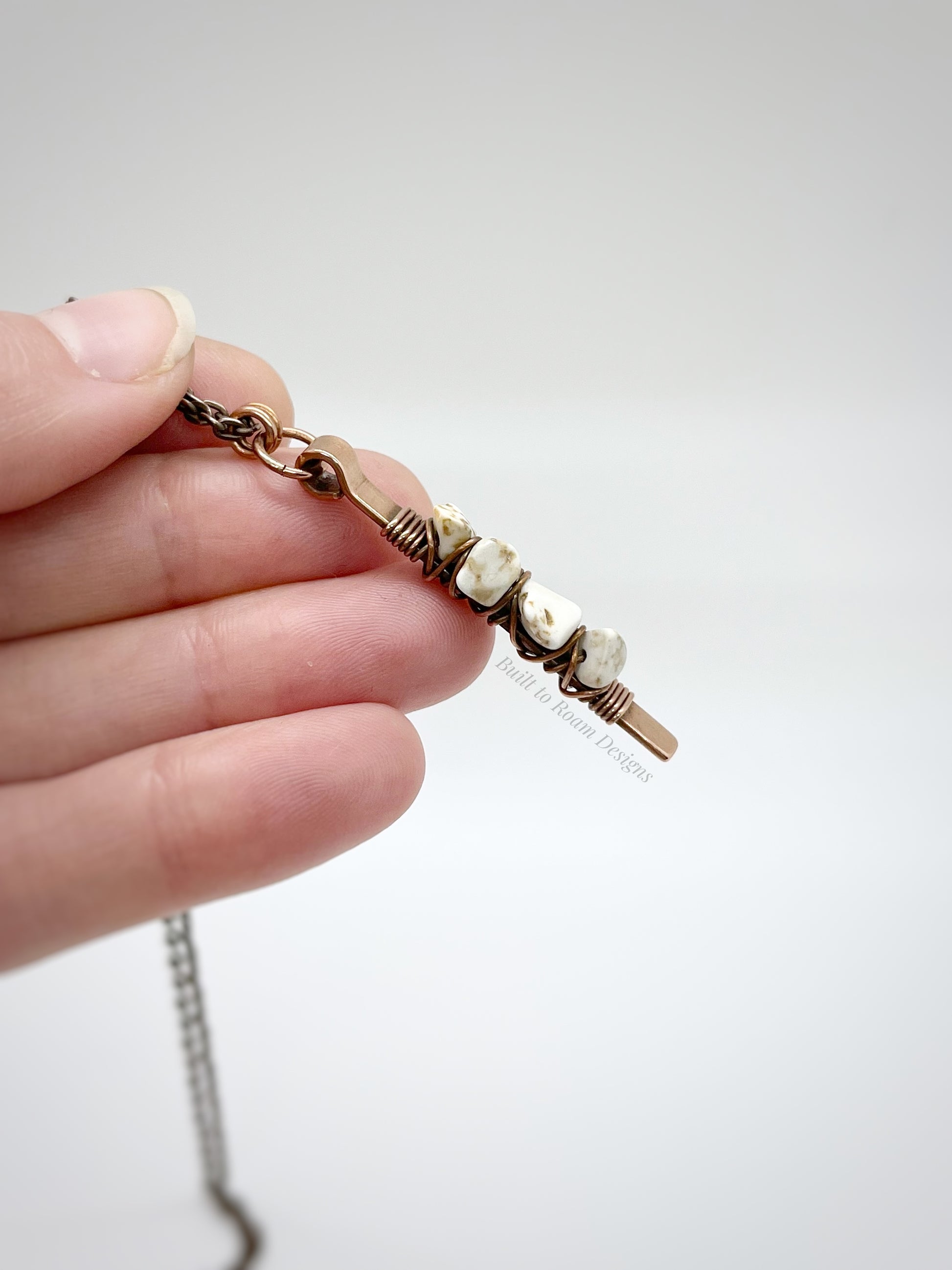 Hand holding a copper bar necklace with white turquoise chip beads on white background - side view - Horizon 
