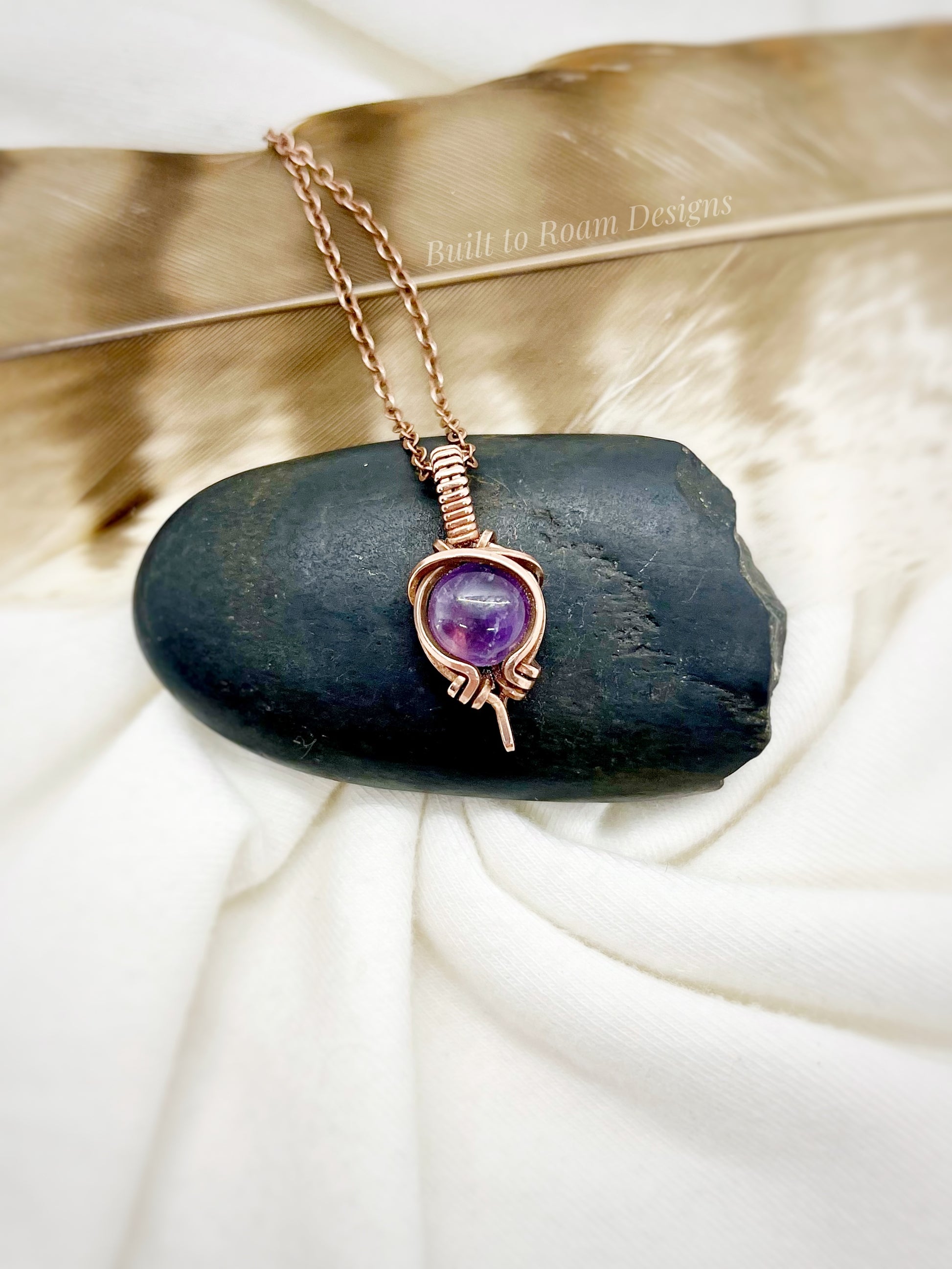 Necklace with a purple amethyst gemstone pendant wrapped in copper on a dark stone surface