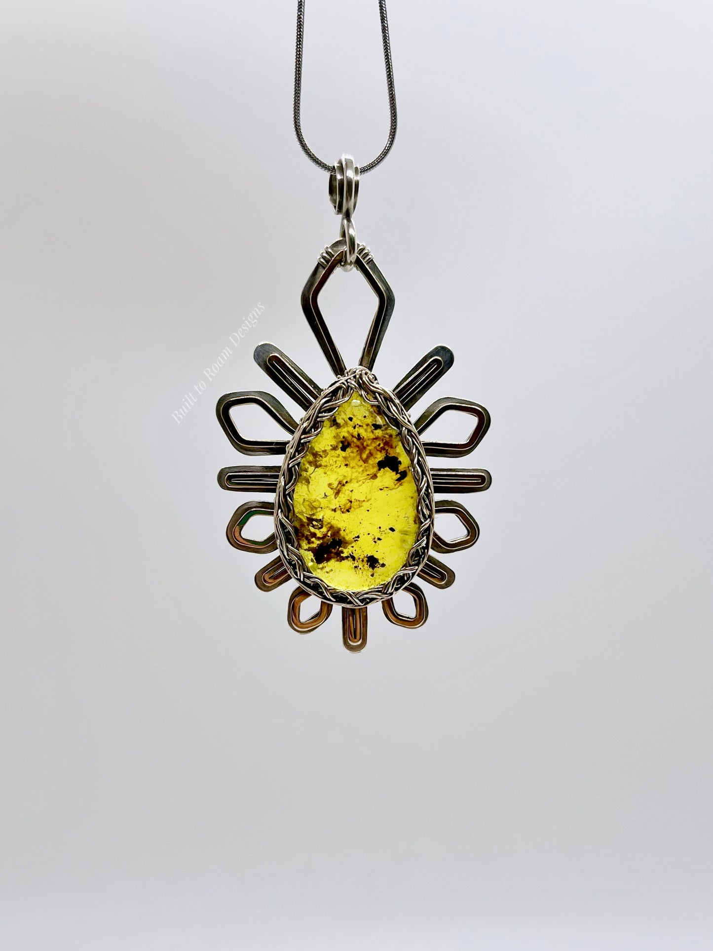 Front view of a silver and bronze star-burst pendant with a golden amber gemstone on a necklace with a white background - Liora
