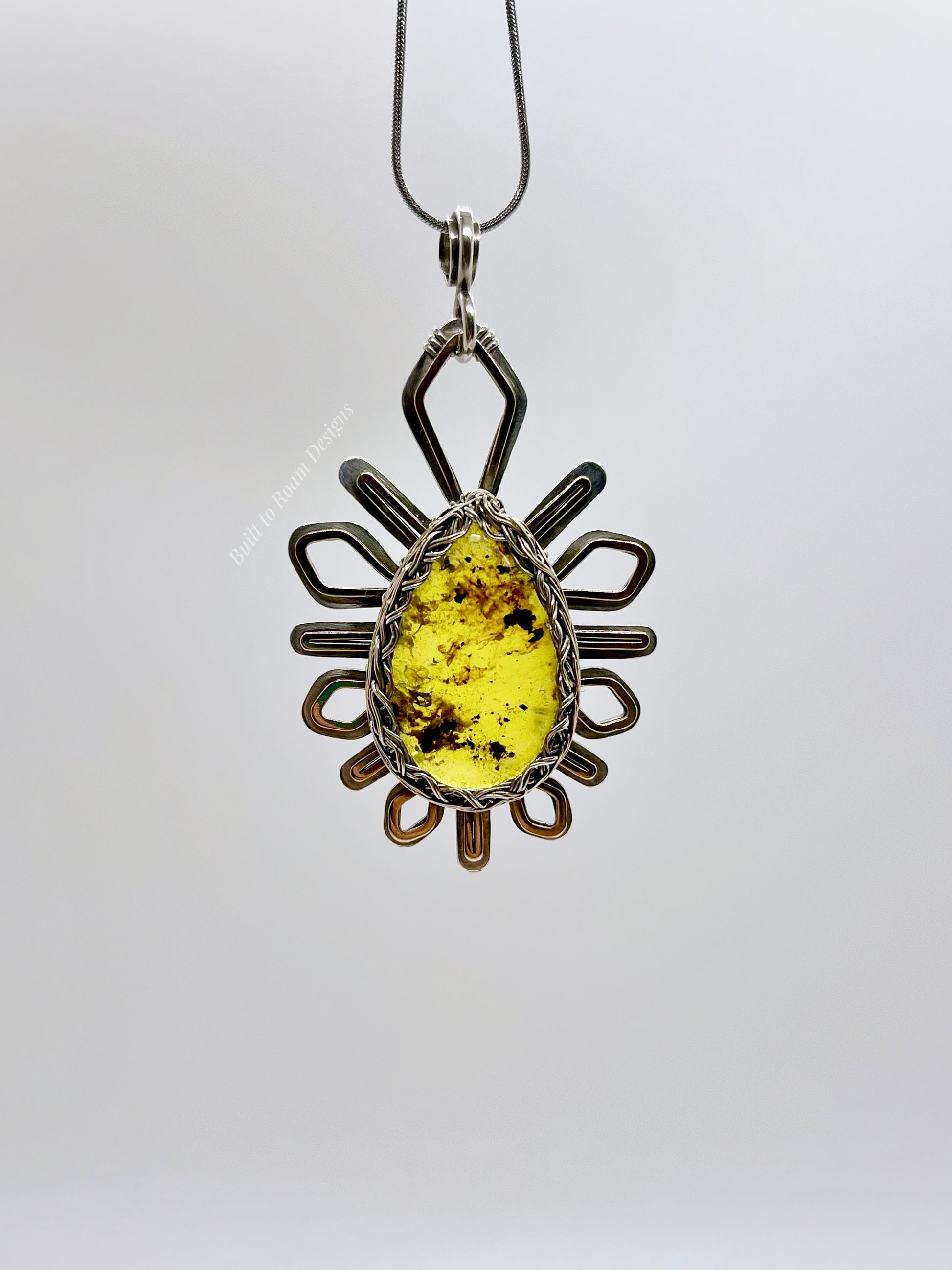 Front view of a silver and bronze star-burst pendant with a golden amber gemstone on a necklace with a white background - Liora