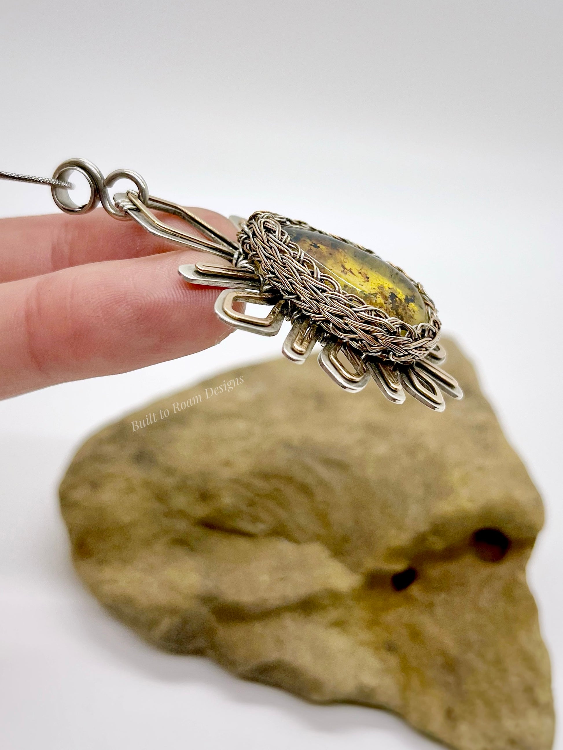 Side view of hand holding a silver and bronze star-burst pendant with a golden amber gemstone - Liora