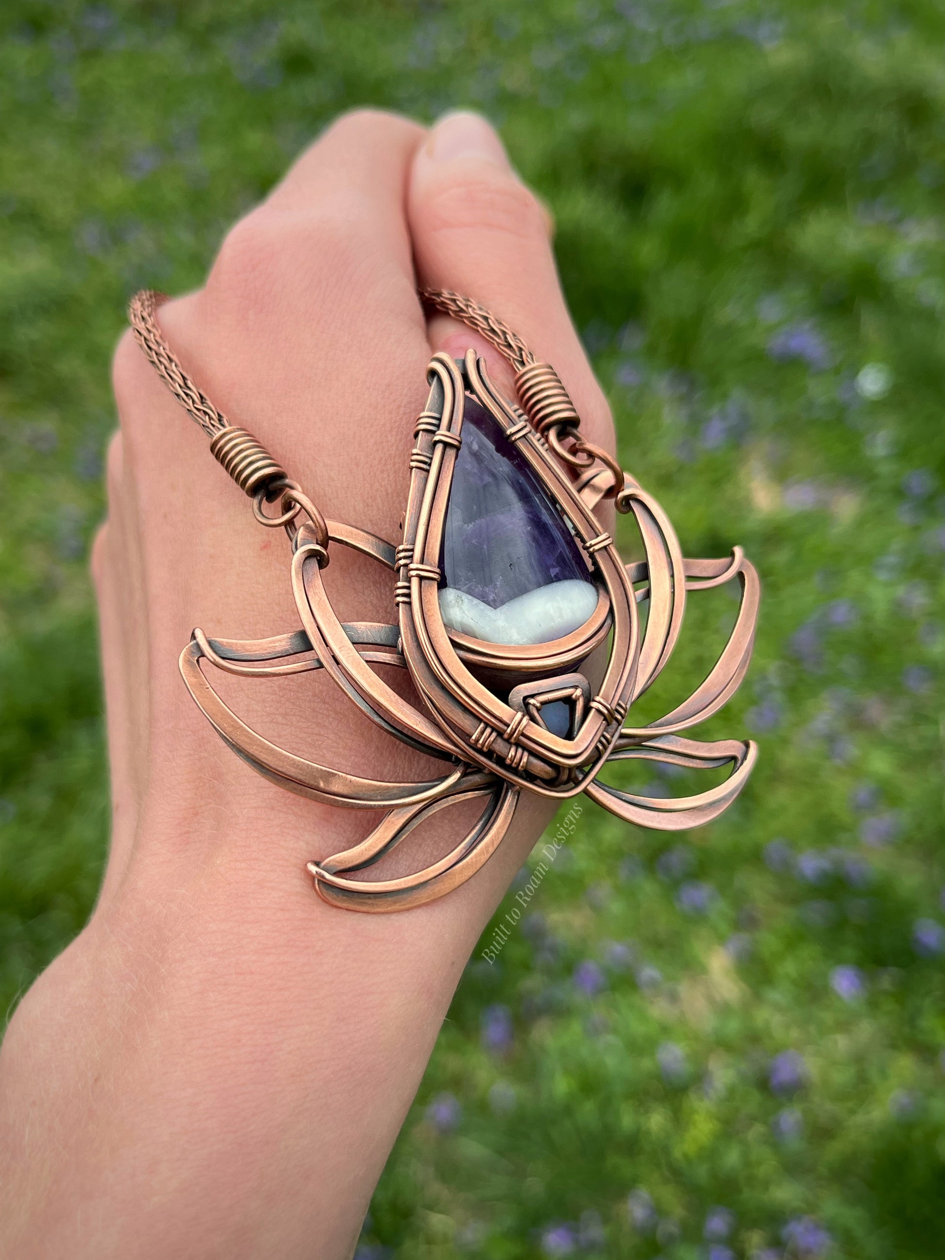 Copper lotus flower Viking knit chain necklace with purple amethyst gemstone held by a hand - side view - Elysian