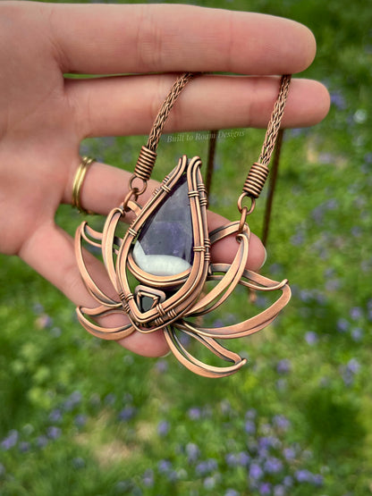 Copper lotus flower Viking knit chain necklace with purple amethyst gemstone held by a hand - side view - Elysian