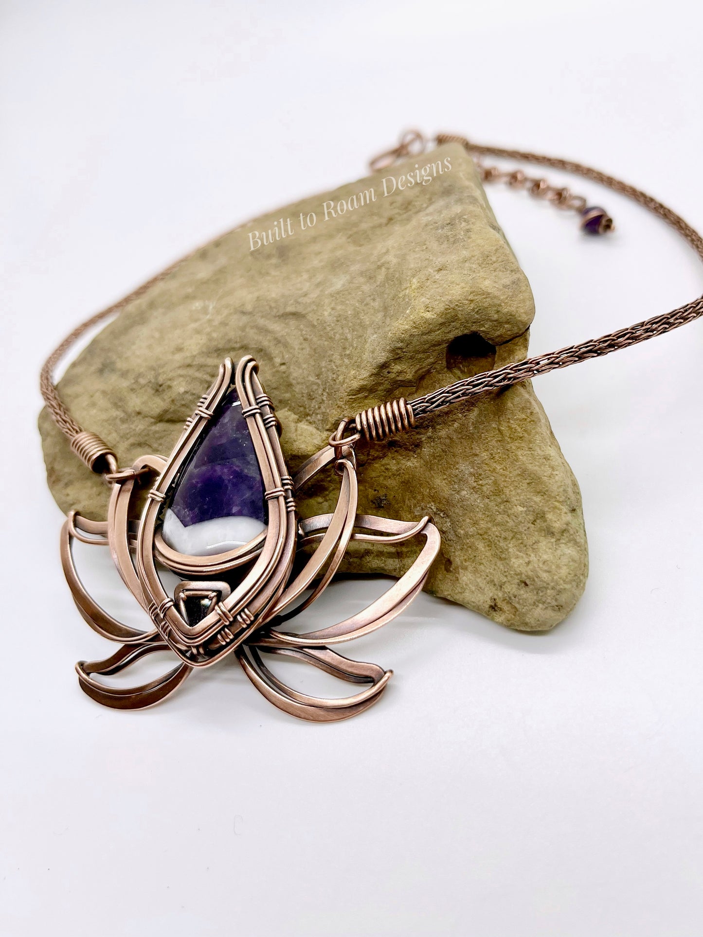 Copper lotus flower Viking knit chain necklace with purple amethyst gemstone on a rock - side view - Elysian