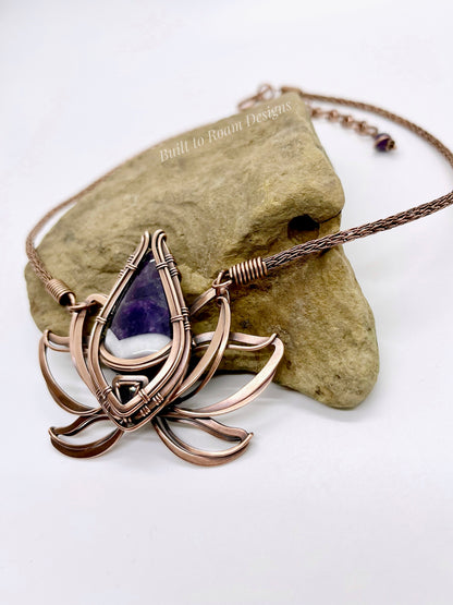 Copper lotus flower Viking knit chain necklace with purple amethyst gemstone on a rock - side view - Elysian