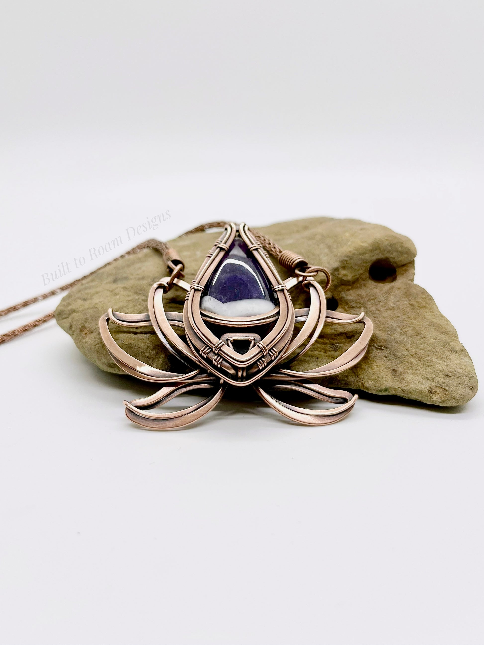 Copper lotus flower Viking knit chain necklace with purple amethyst gemstone on a rock - side view - Elysian