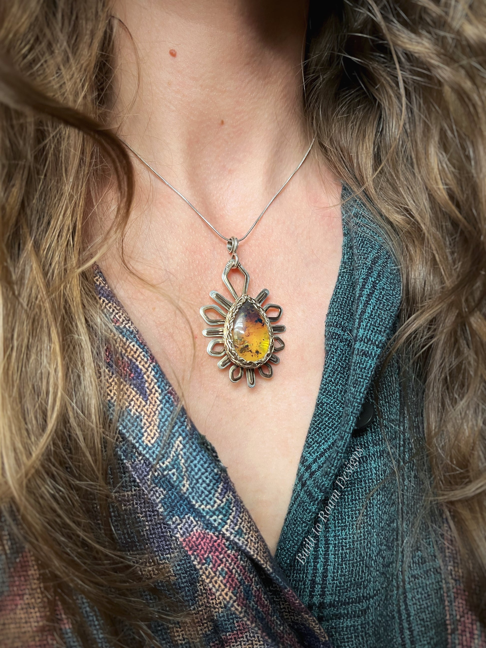 Silver and bronze necklace with a starburst-shaped pendant featuring a yellow amber gemstone worn by a person with long hair - Liora